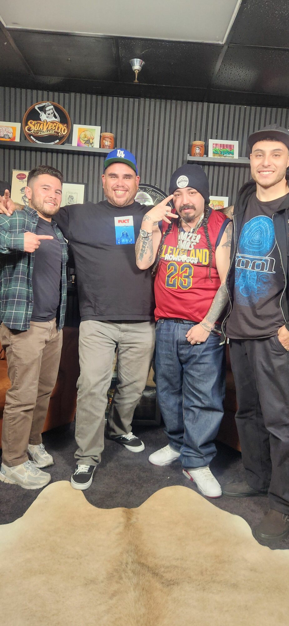 Four people standing in a room with shelves and books, posing for a photo, some making peace signs.