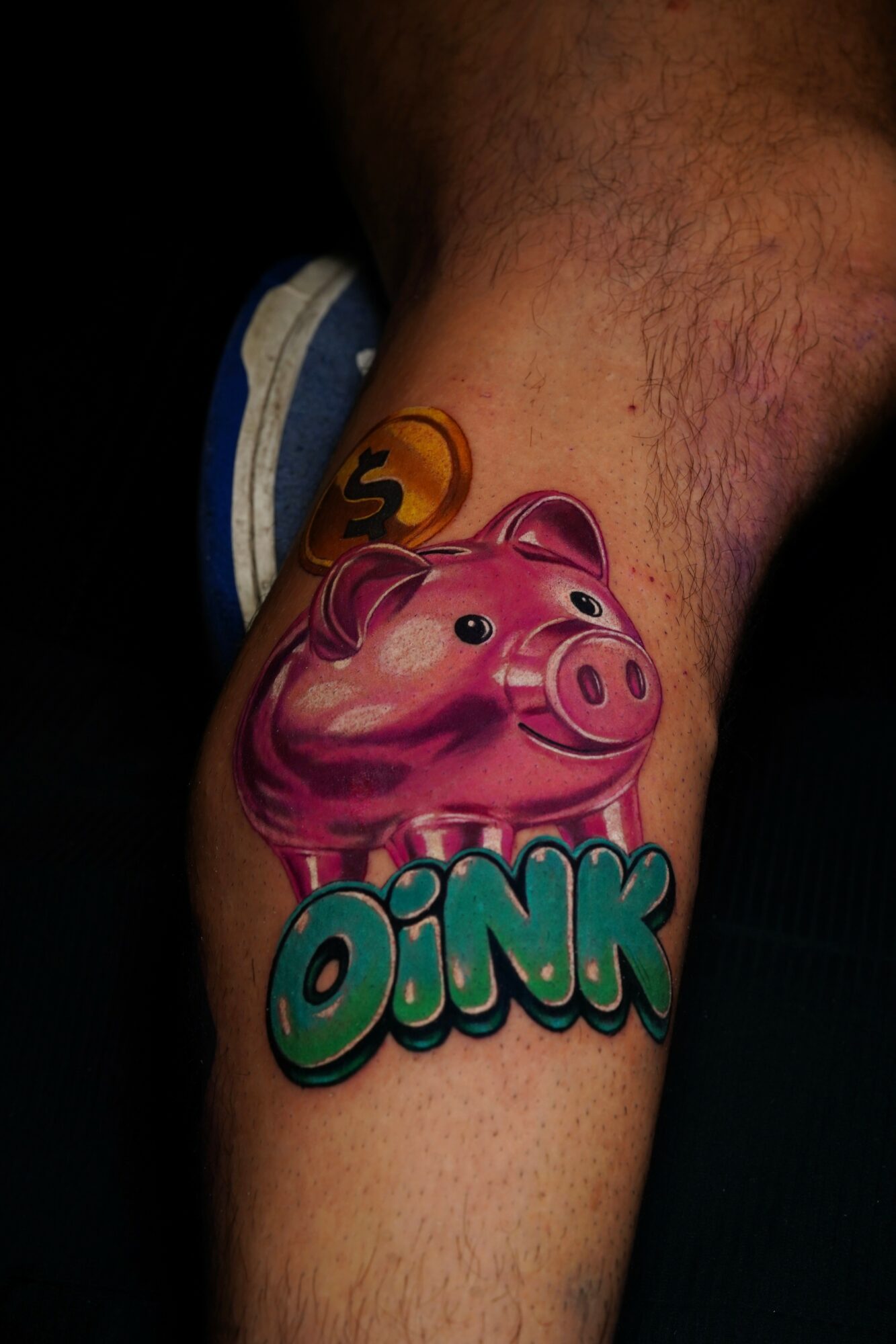 Pink pig cartoon tattoo with the word 'OINK' on a person's arm.