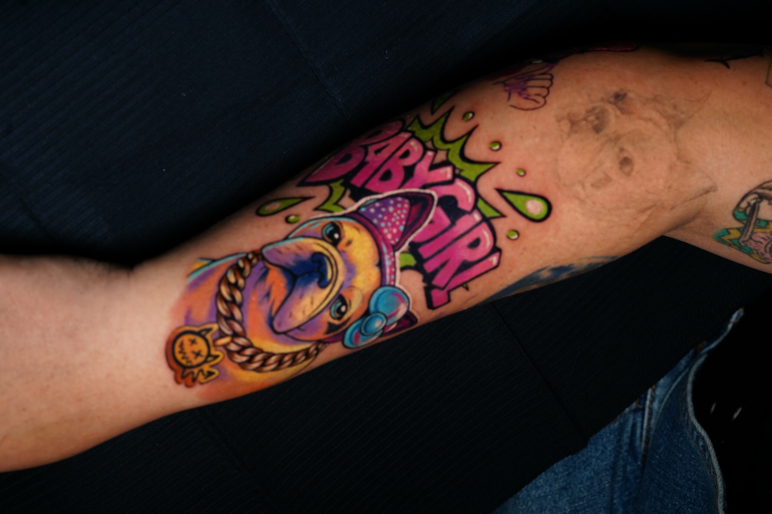 Colorful tattoo of a clown with a pumpkin, surrounded by text and decorative elements on a person's arm.
