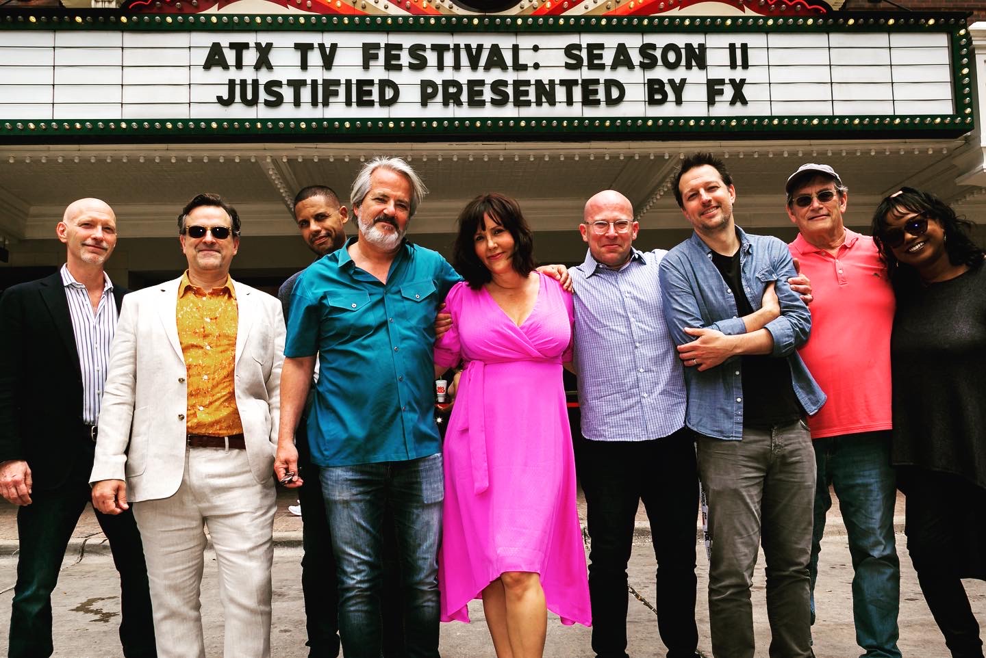 Group of nine people standing in front of a marquee with a sign about ATX TV Festival, some smiling, some with arms crossed.