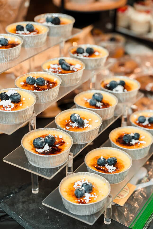 Small dessert cups filled with custard and topped with blueberries and syrup, arranged on a multi-tiered display stand.