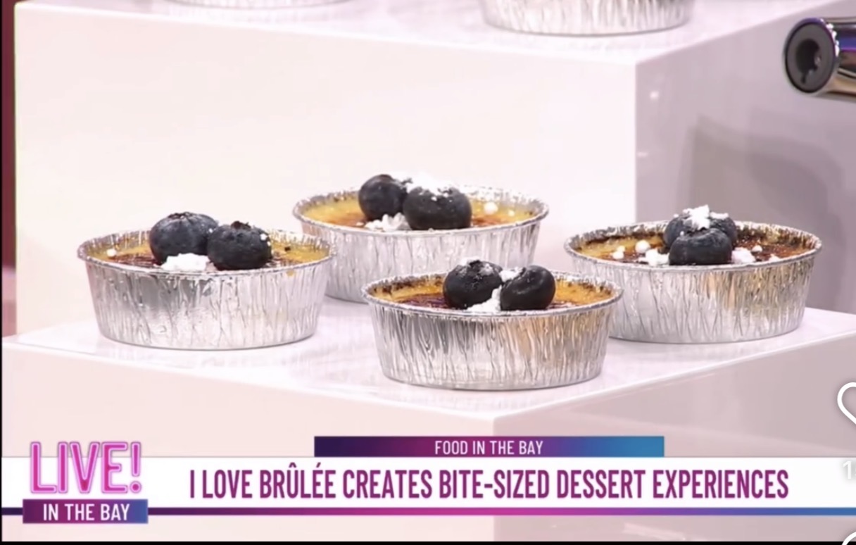 Five small dessert tarts topped with blueberries on a white surface, with a pink and white background.