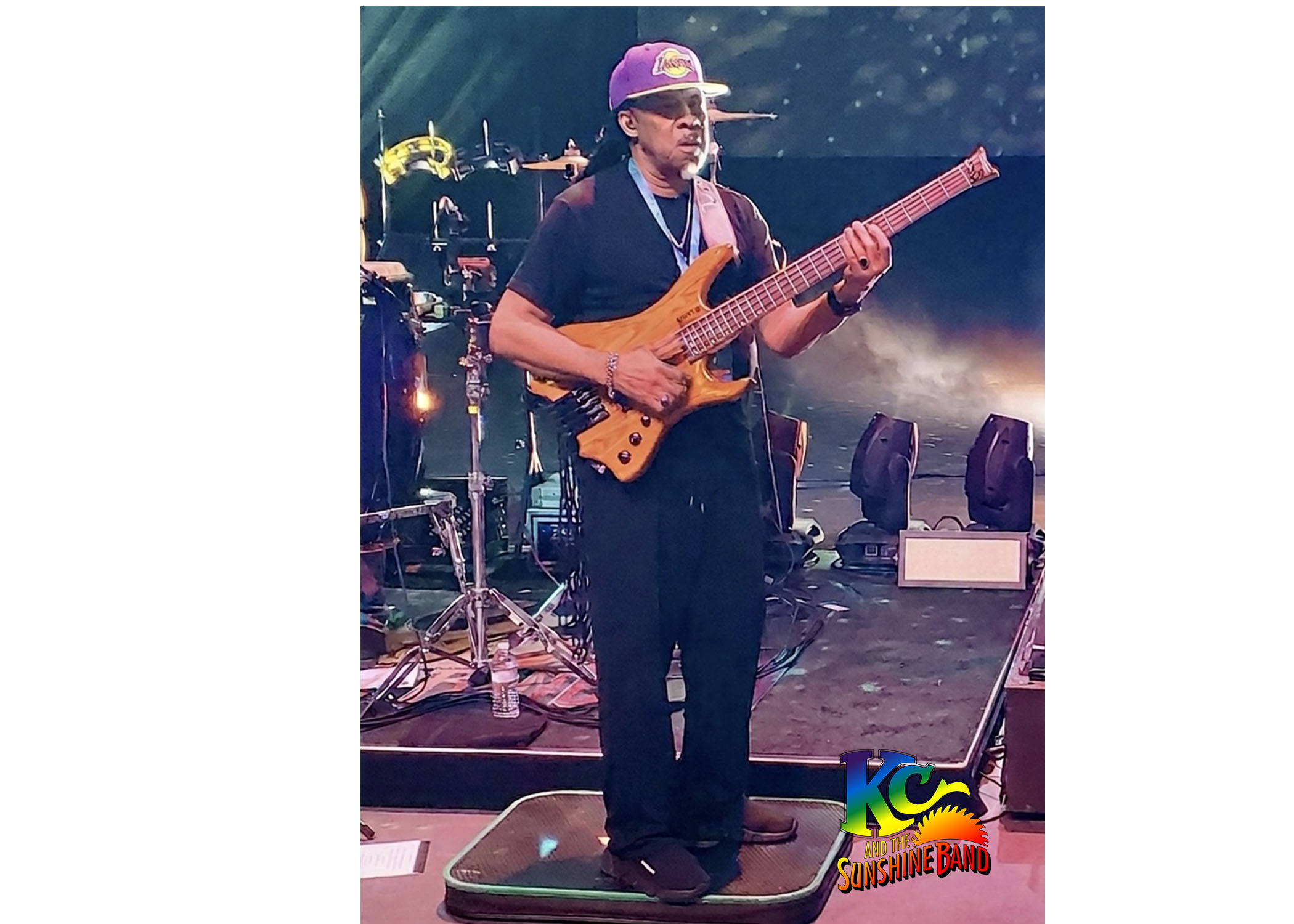 Person playing an electric guitar on stage with musical equipment and colorful lighting in the background.