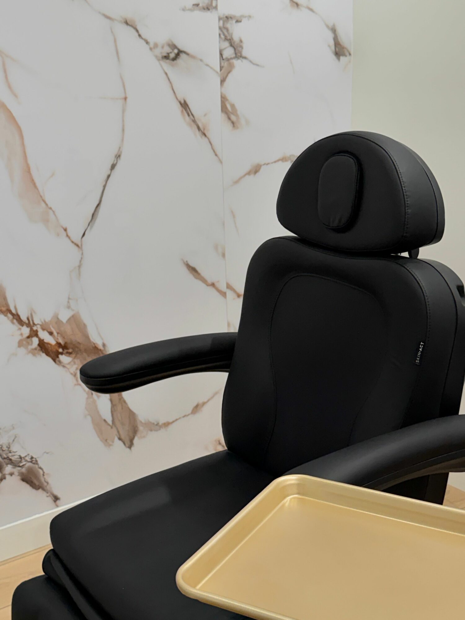 Office chair with black backrest and armrest, beige tray, and marble floor.