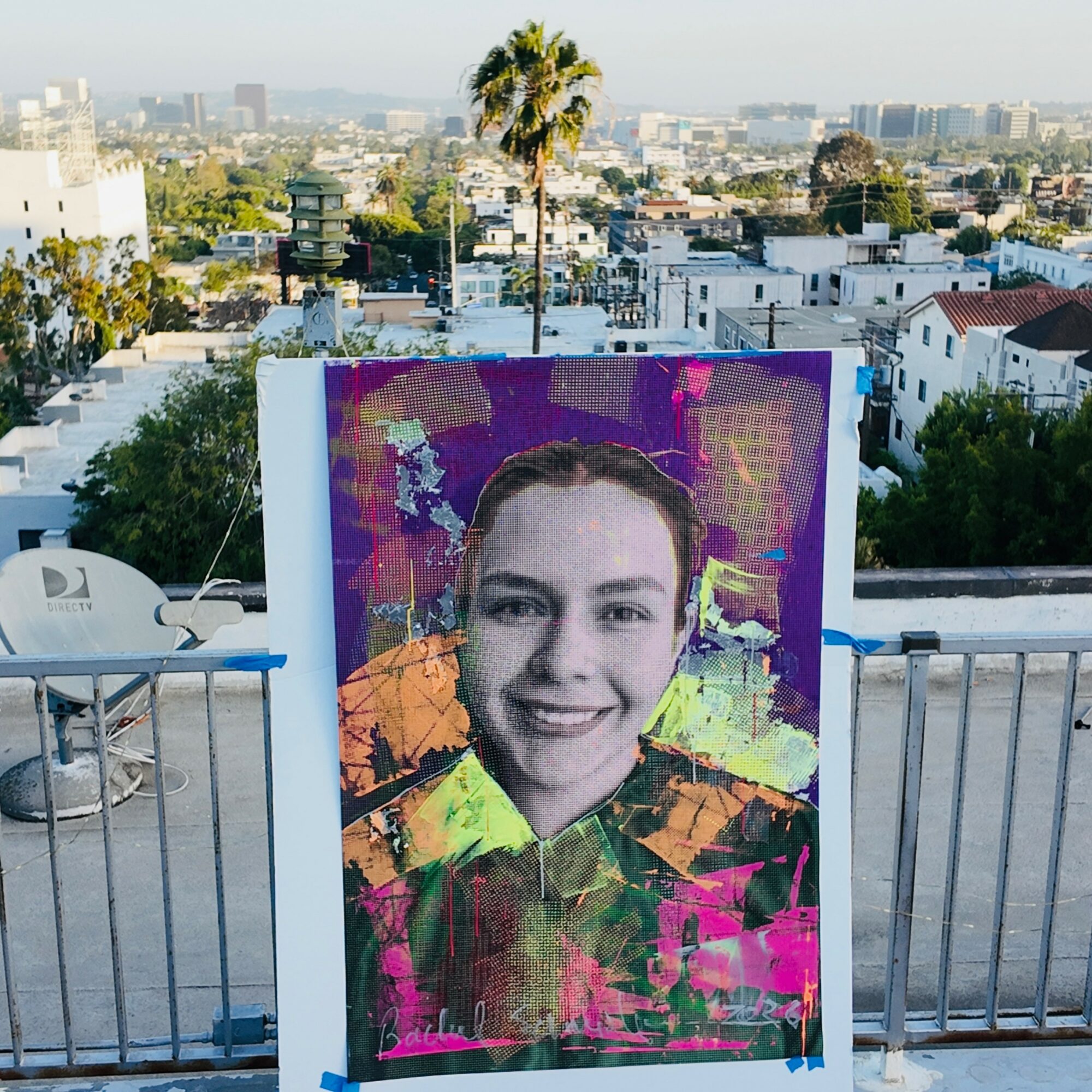 A colorful digital portrait of a smiling person with a cityscape background, displayed outdoors on a rooftop.