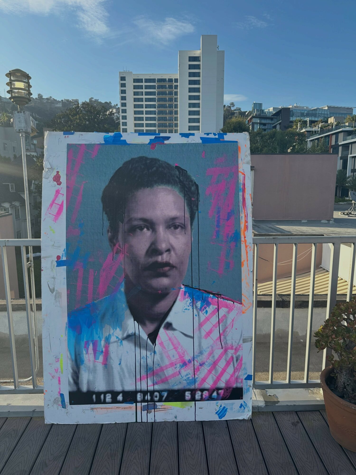 Portrait of a young man with short dark hair, wearing a striped shirt, against a colorful background with pink and blue paint splatters.