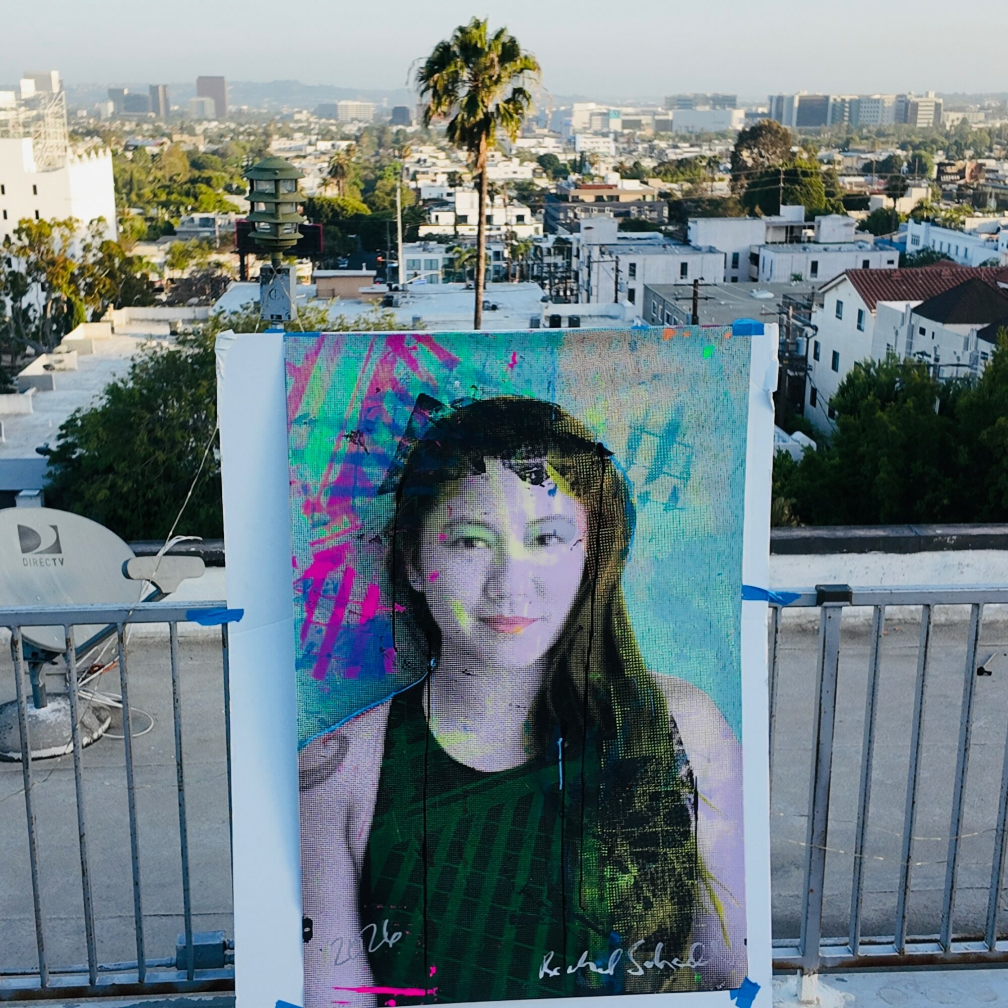Large poster of a woman with long dark hair, wearing a black top, against a colorful background, on a rooftop.