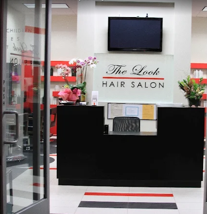 Reception desk with flowers and a sign reading 'The Look Hair Salon' inside a salon, viewed through glass doors.