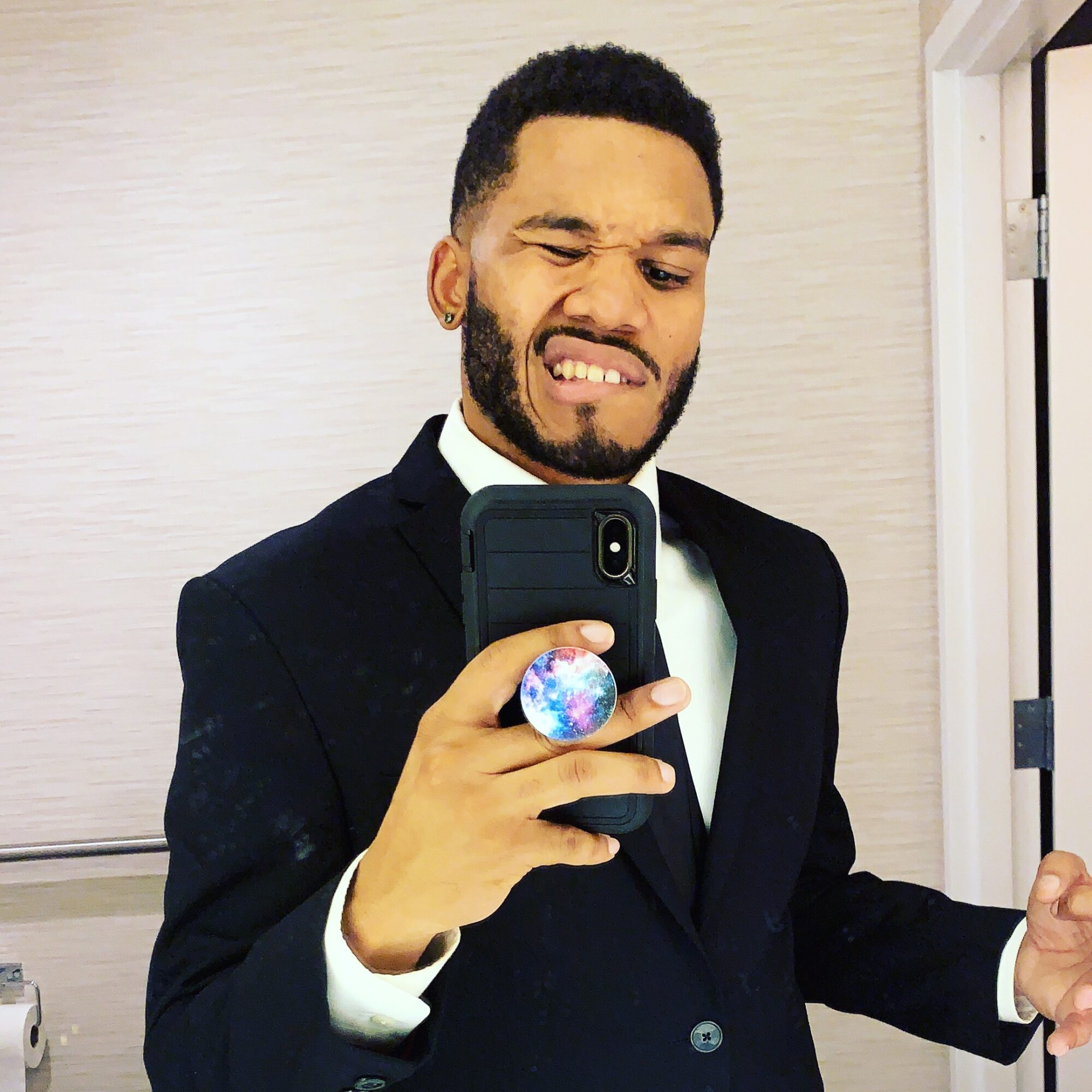Man in a suit taking a selfie, making a grimace, in front of a mirror.