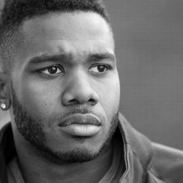 Close-up of a young man with short hair and a beard, looking serious, in black and white.