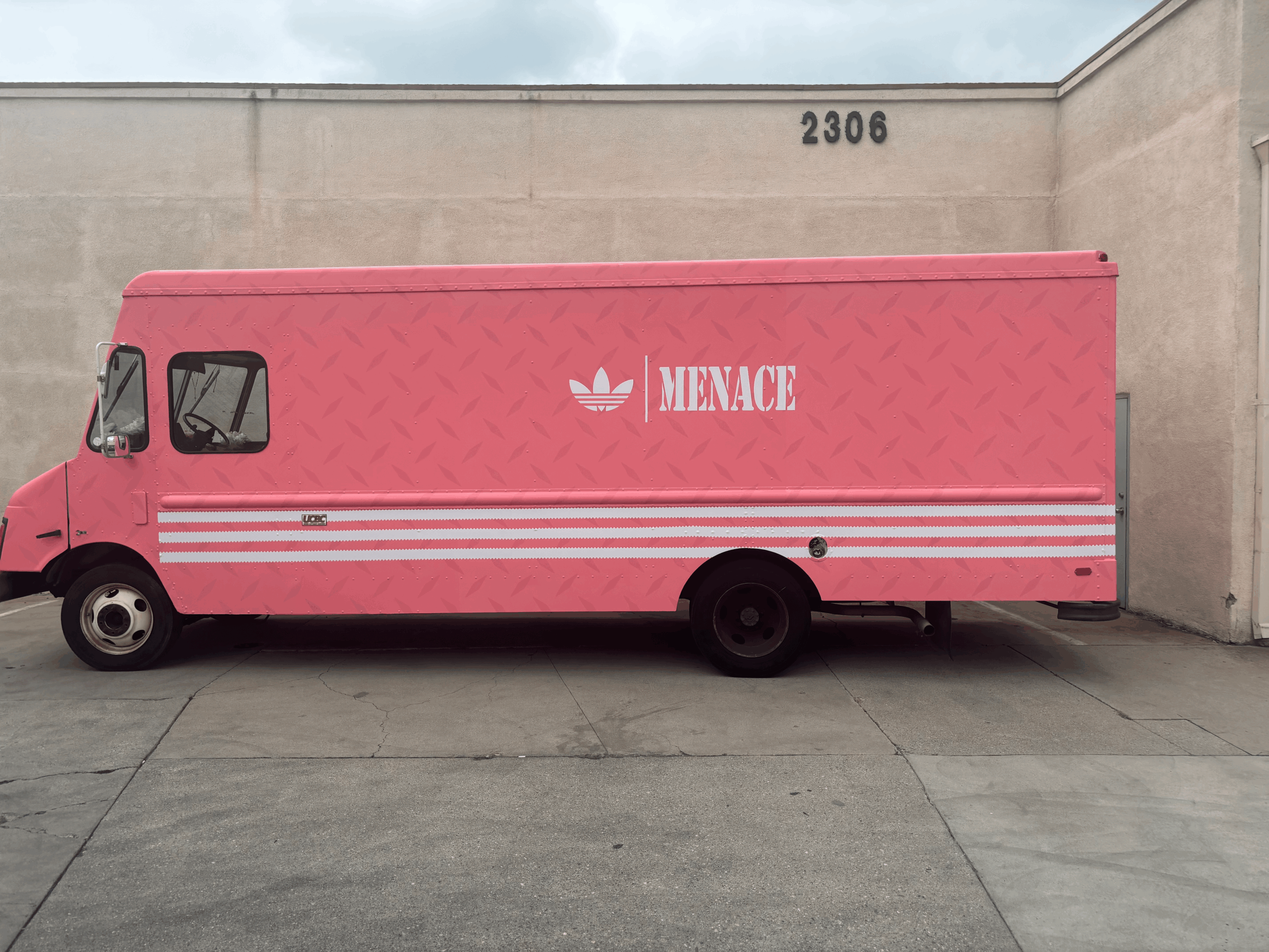 Pink delivery truck with white stripes and 'MENACE' logo parked against a wall.