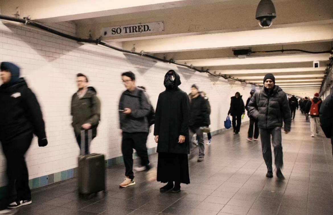 People walking in an underground passage with a sign that says 'SO TIRED.'