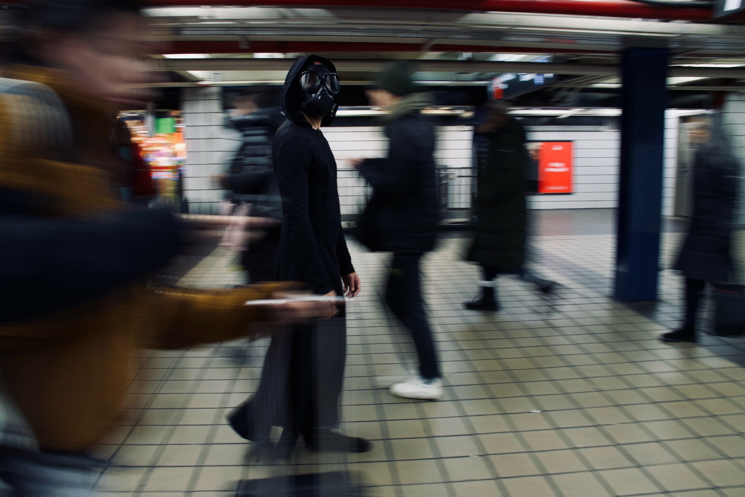 People waiting at a subway station platform, some standing and some walking, with tiled floor and station background.