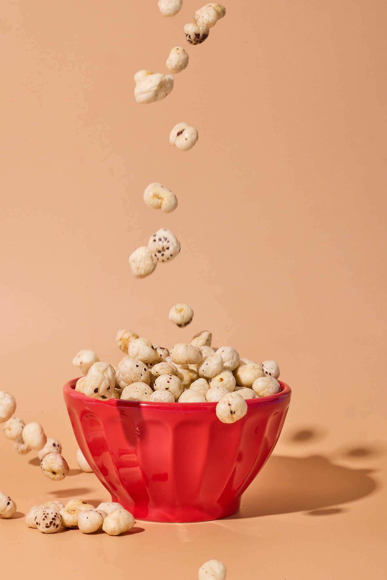 Popcorn falling into a red bowl against a beige background.