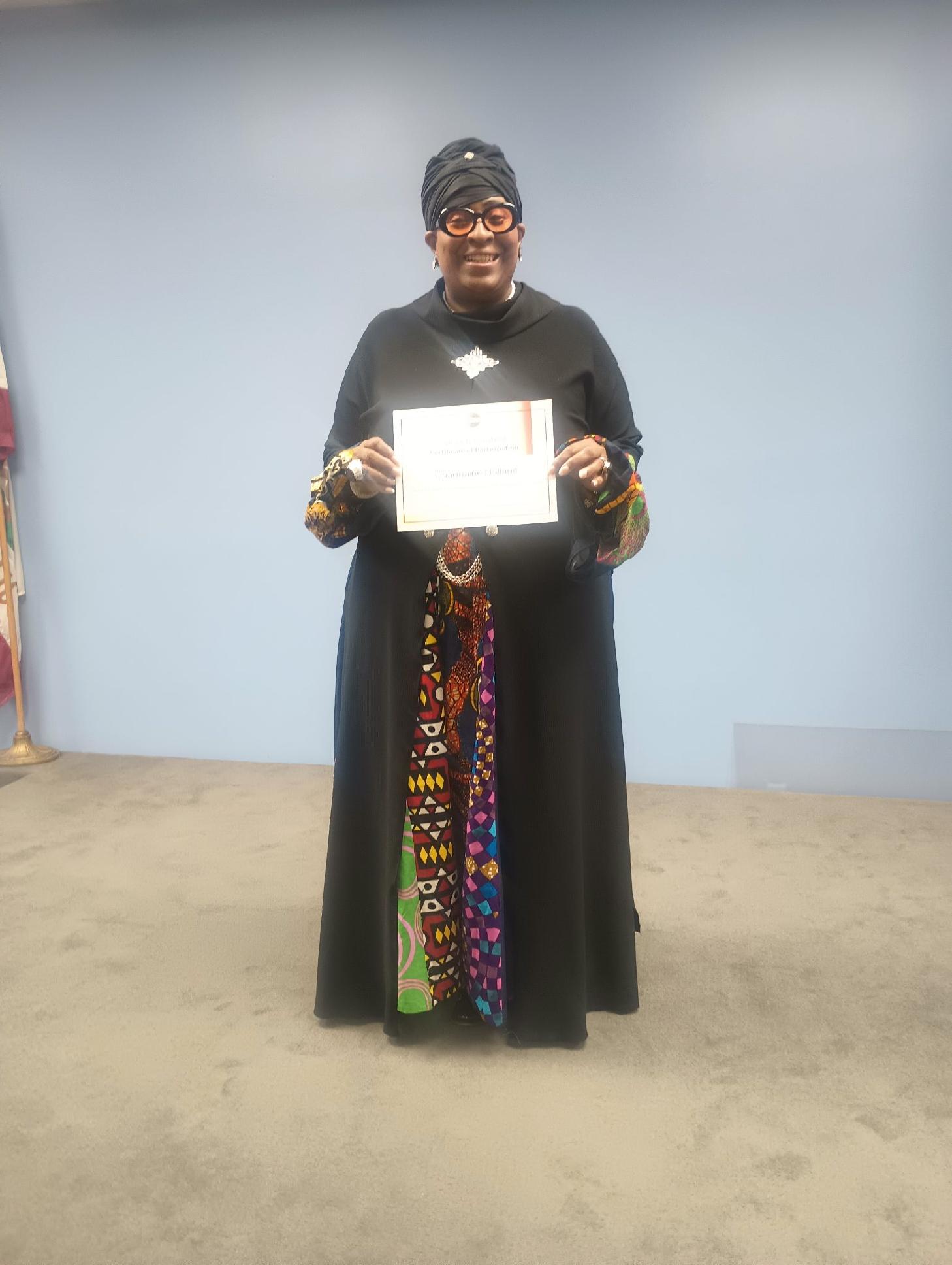 Person in black dress holding a certificate, standing on a beige floor against a light blue wall.