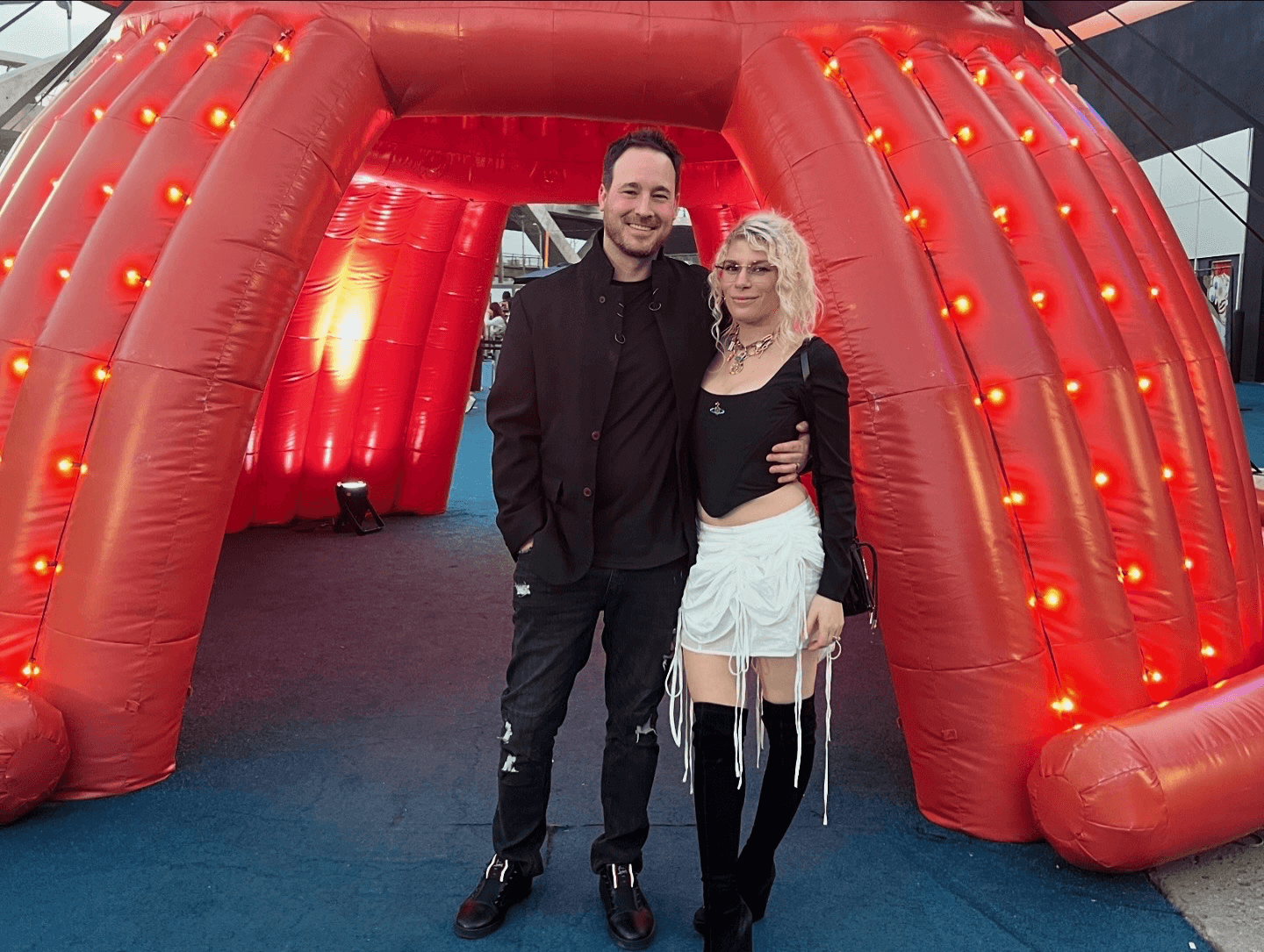 Two people stand in front of a large red inflatable structure with lights, smiling at the camera.