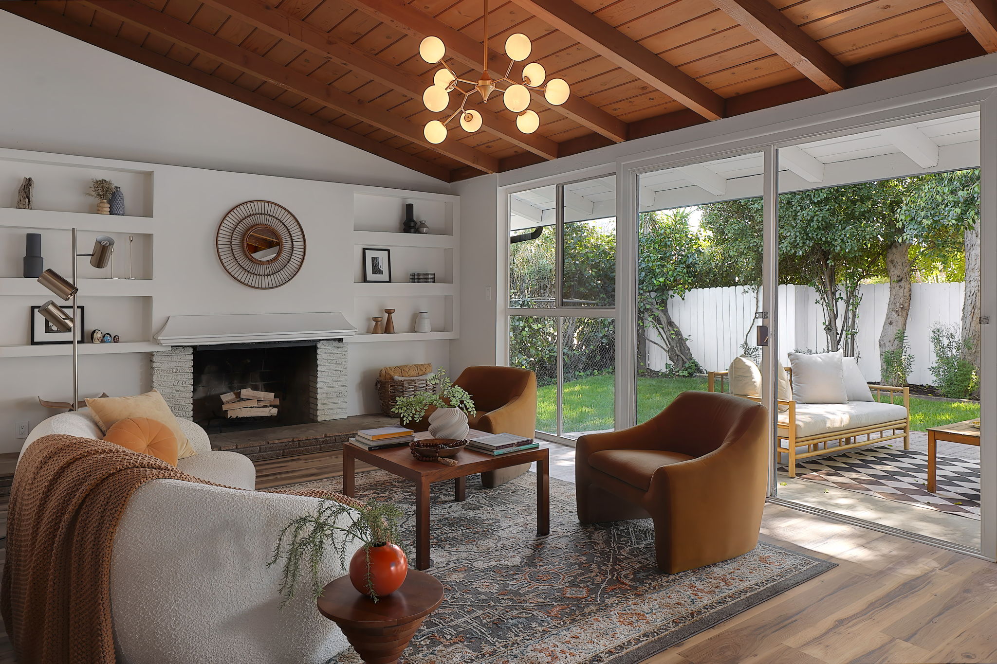 Living room with large windows, white shelves, fireplace, wooden ceiling, and seating area with chairs and a coffee table.