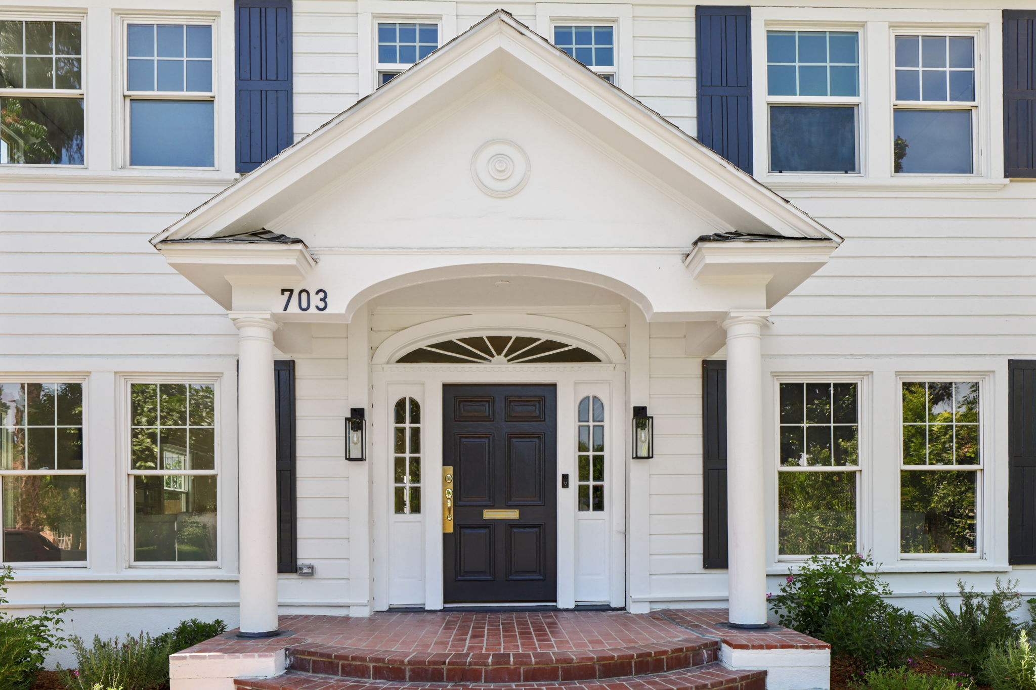 Front entrance of a white house with a black door, porch, and columns, with house number 703 visible.