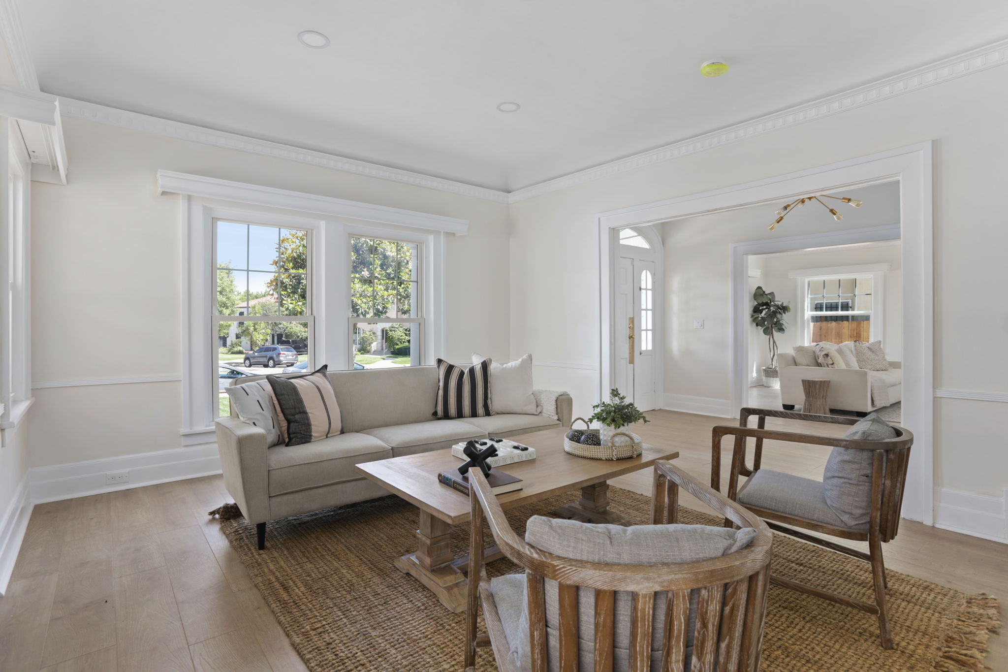 Living room with white walls, large windows, sofa, armchair, coffee table, and a rug, with a view into another room.