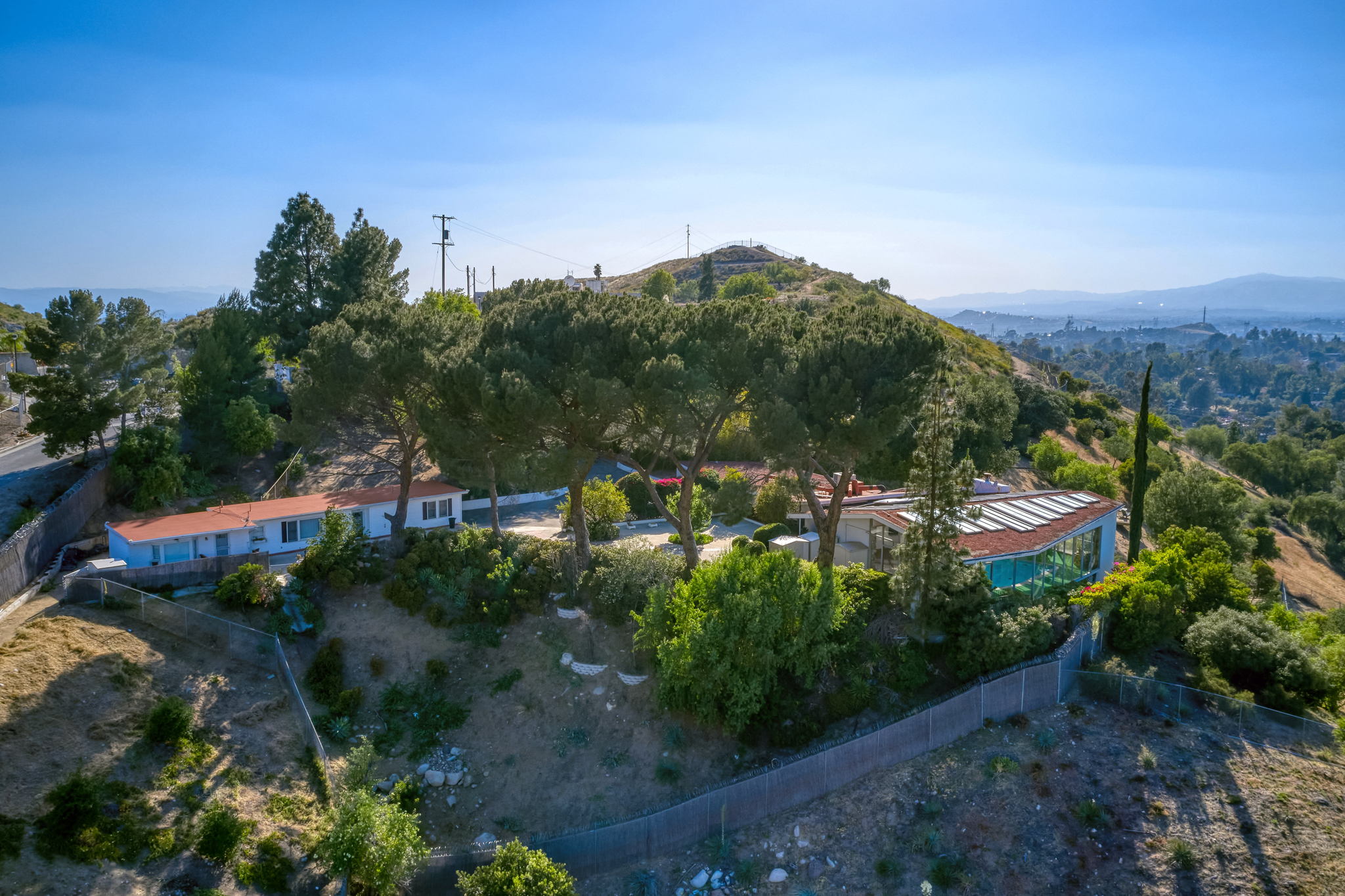 Hilly landscape with trees, buildings, and a clear blue sky, viewed from an elevated position.