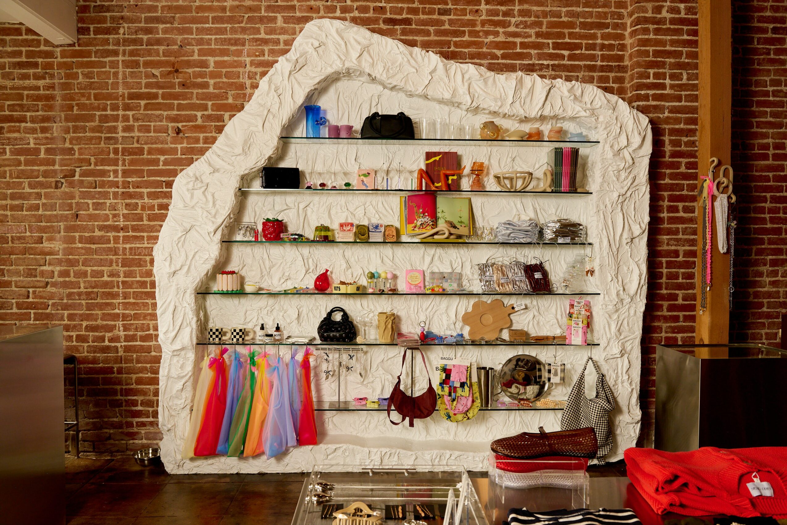 Display shelf with colorful items against a brick wall, with chairs and a table nearby.