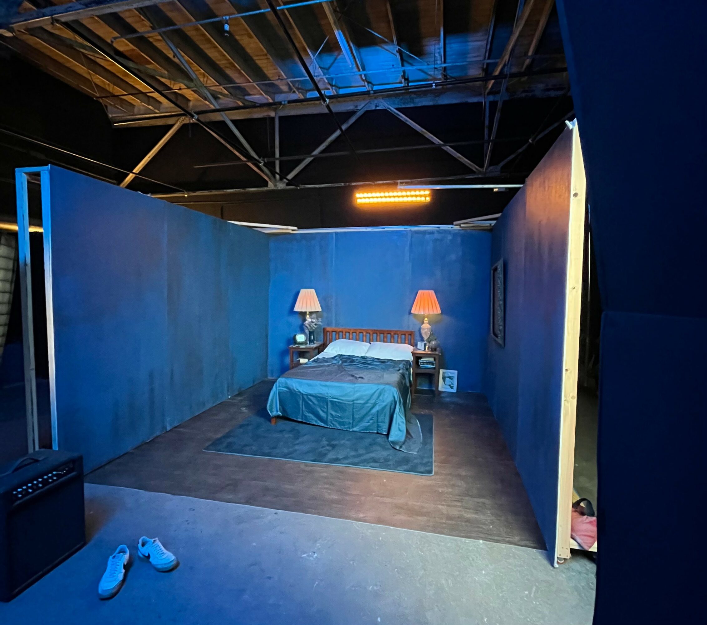 A bedroom with a bed, two lamps, and blue walls, viewed from the doorway. Shoes are on the floor outside.