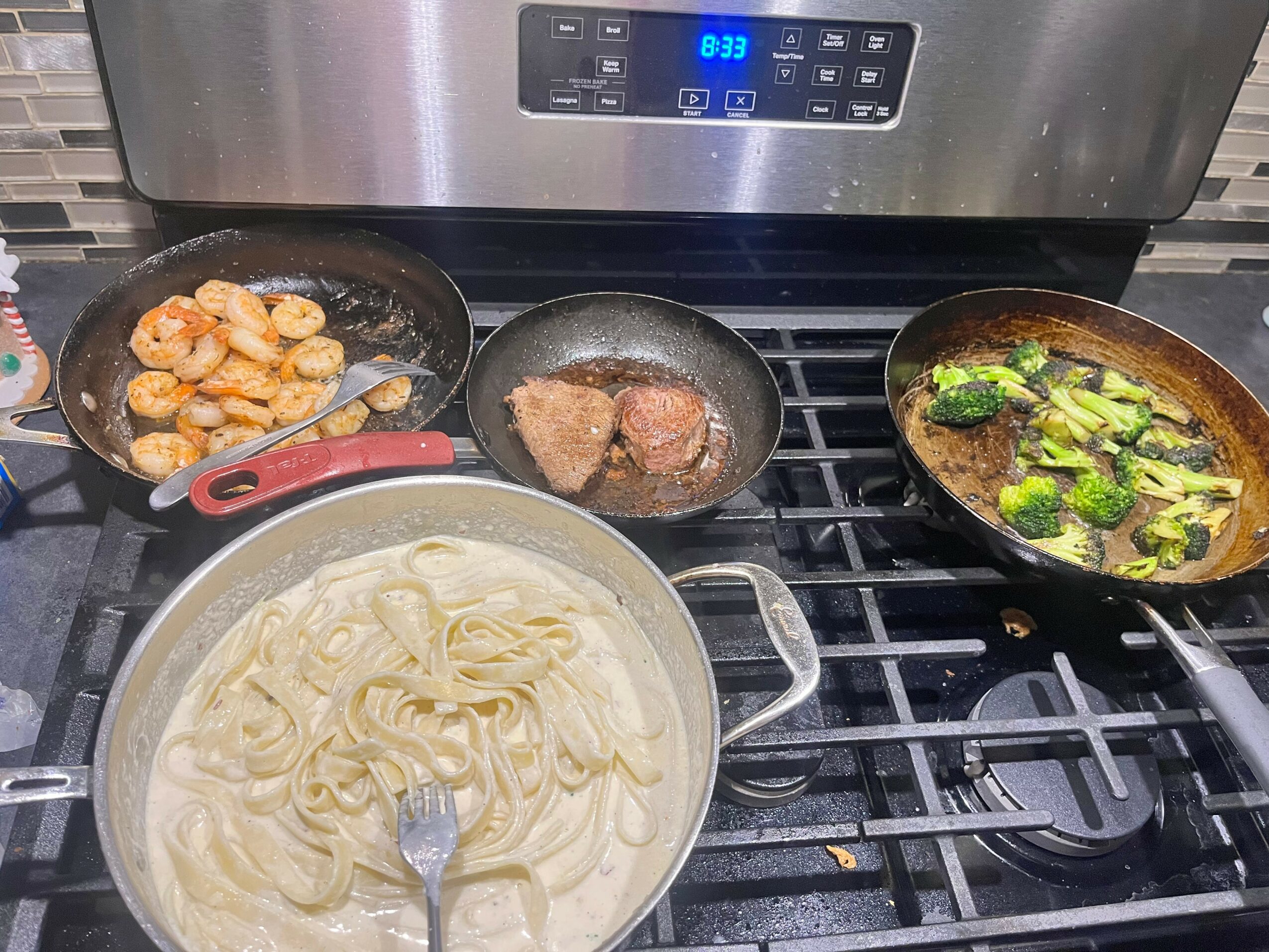 Cooking on a stove with a pot of noodles, a pan of meat, and a pan of vegetables, with a digital clock display.