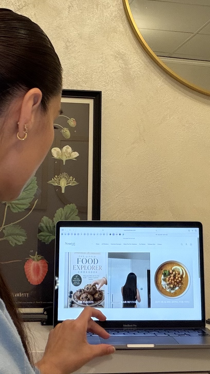 Person using a laptop in a room with a framed botanical print and a round mirror on the wall.