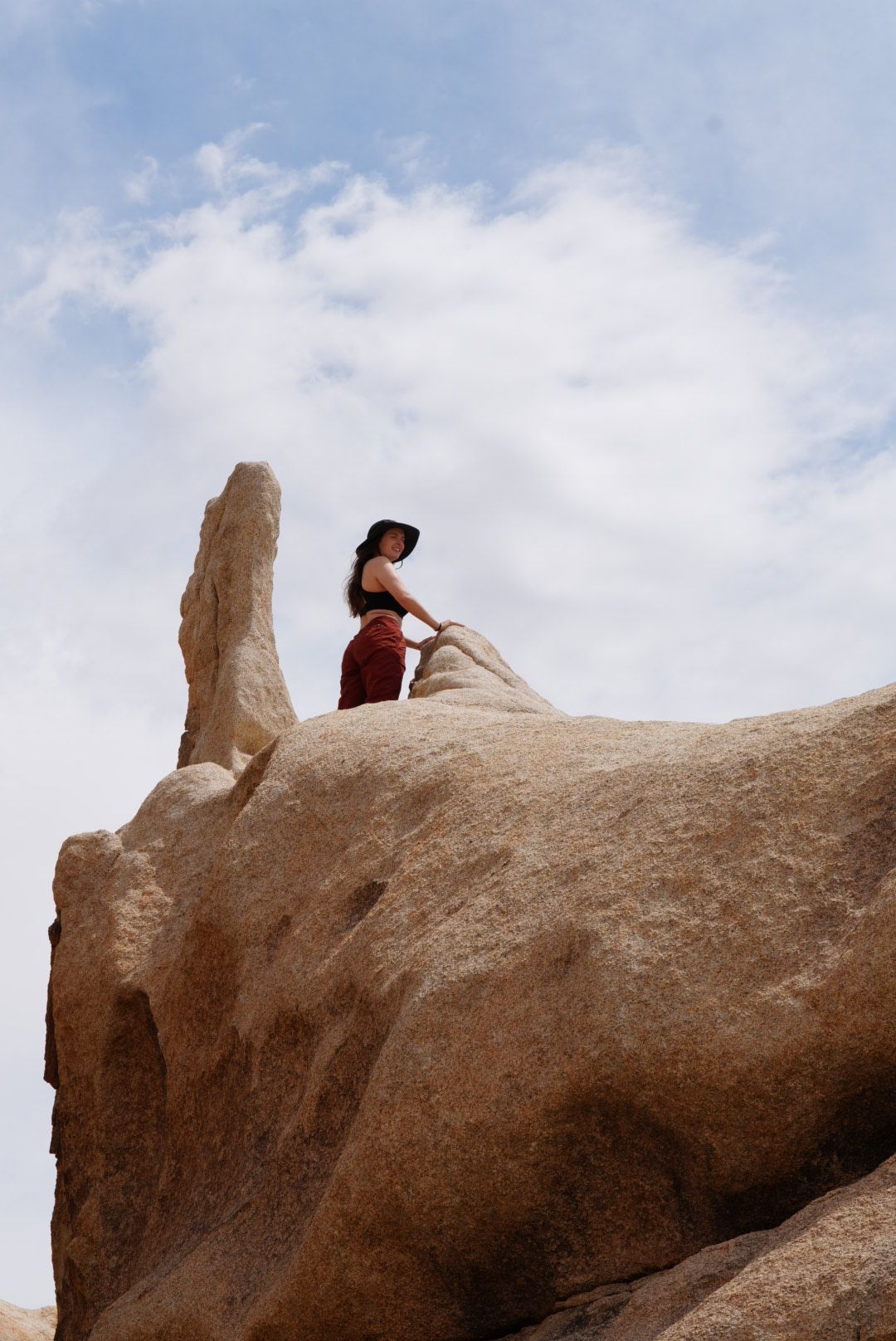 Person sitting on a large rock formation against a cloudy sky, viewed from the side.