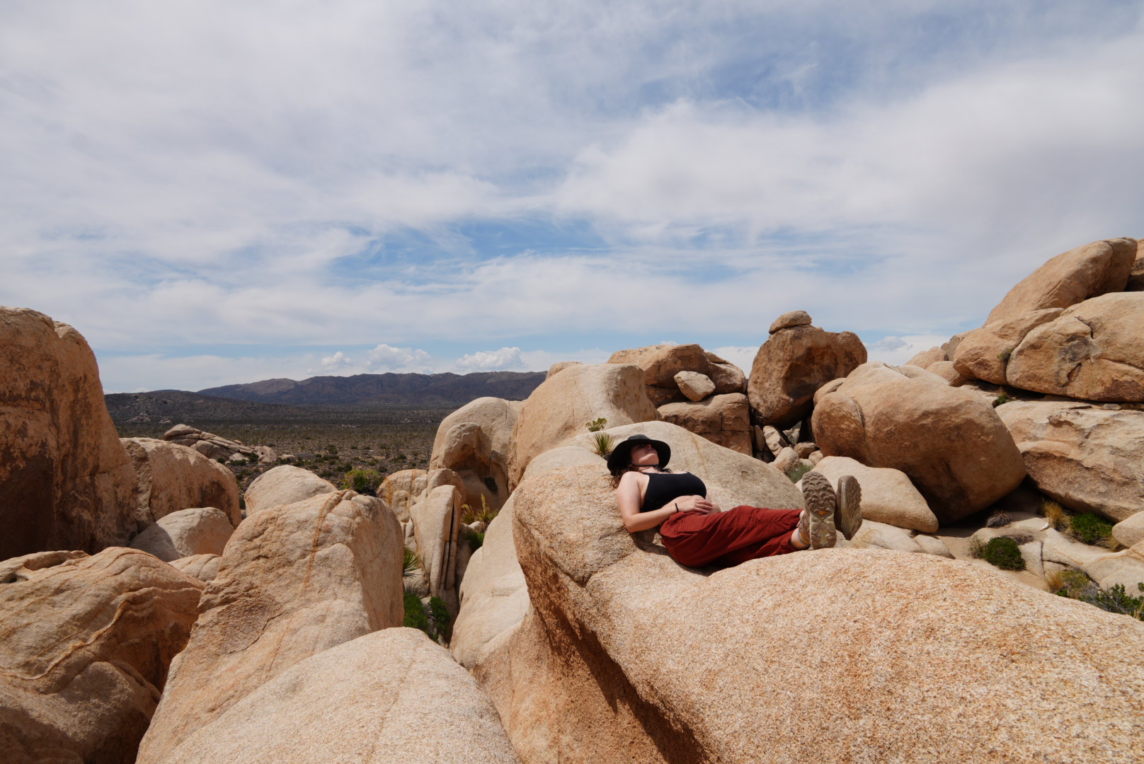 Person lying on large rocks outdoors with a cloudy sky and distant mountains in the background.