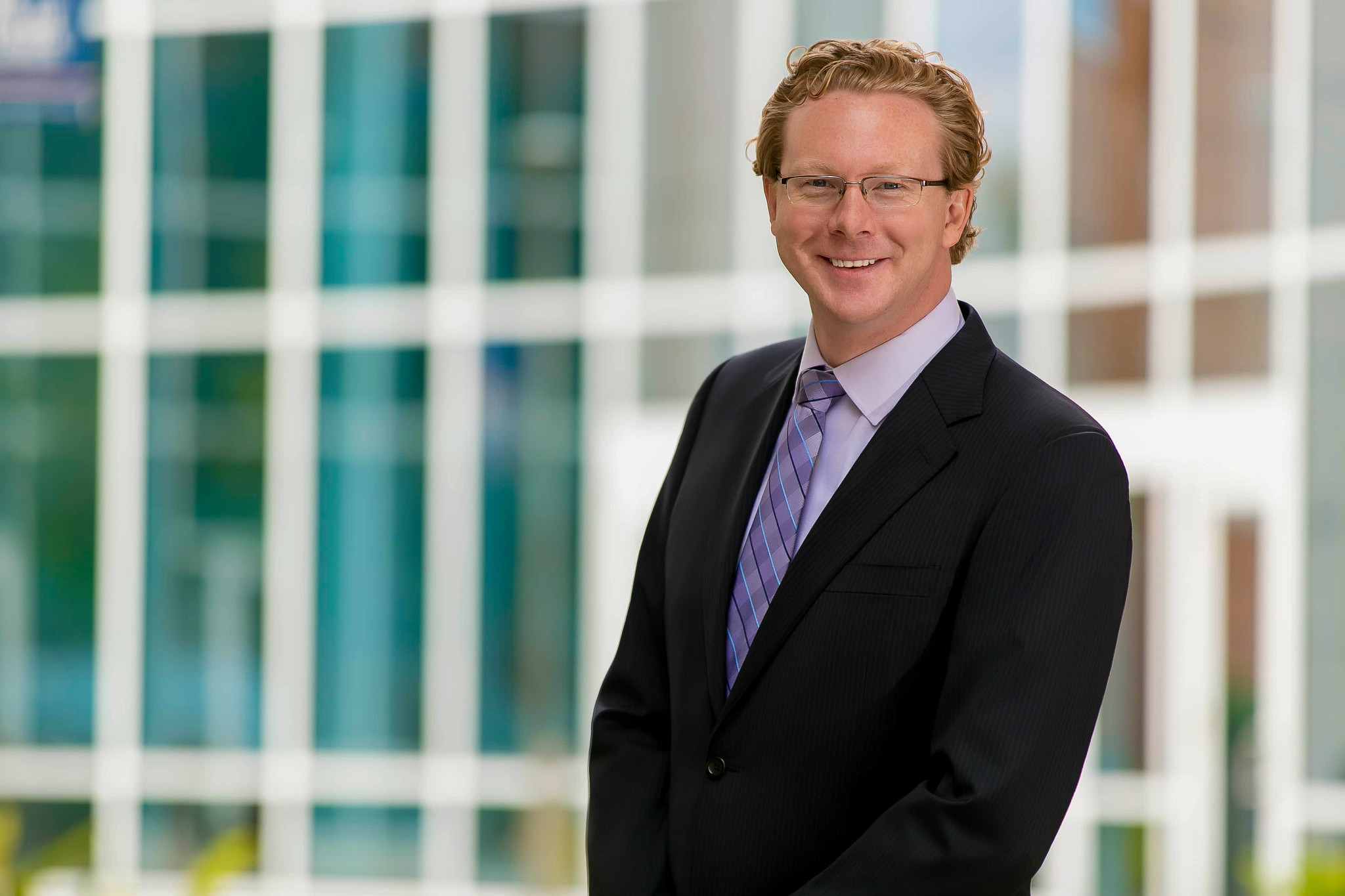 Man in a suit smiling outdoors with a modern building background