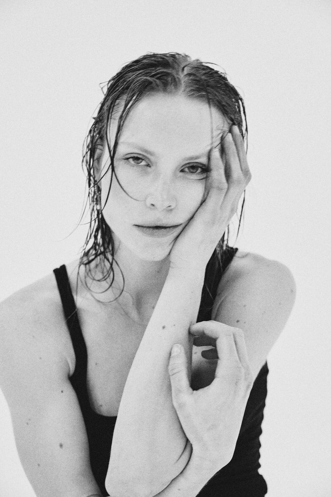 Black and white portrait of a woman with wet hair, touching her face with one hand, wearing a sleeveless top.
