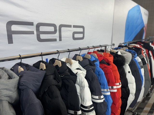 Clothing rack with jackets and coats in various colors, in front of a wall with the word 'Fera'.