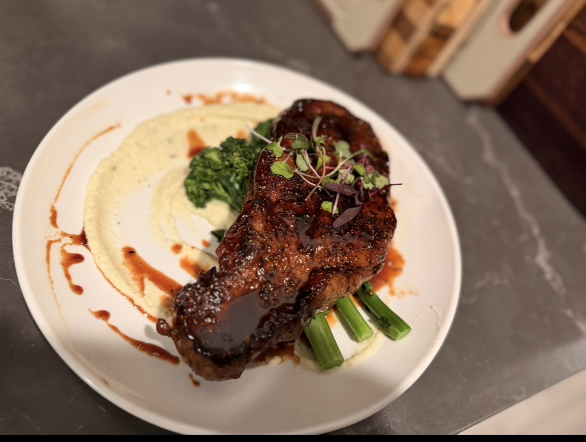 Grilled meat with green vegetables, mashed potatoes, and sauce on a white plate.