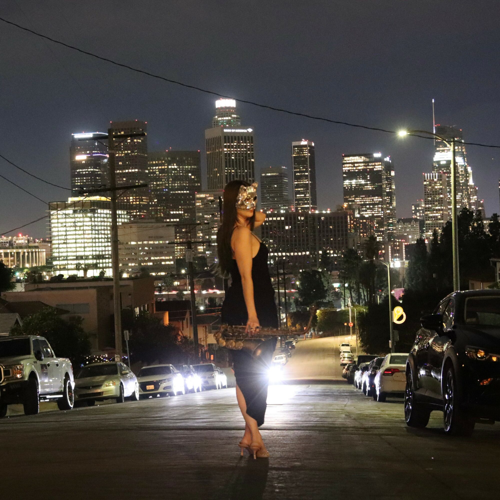 Woman standing on a city street at night with illuminated skyscrapers in the background.