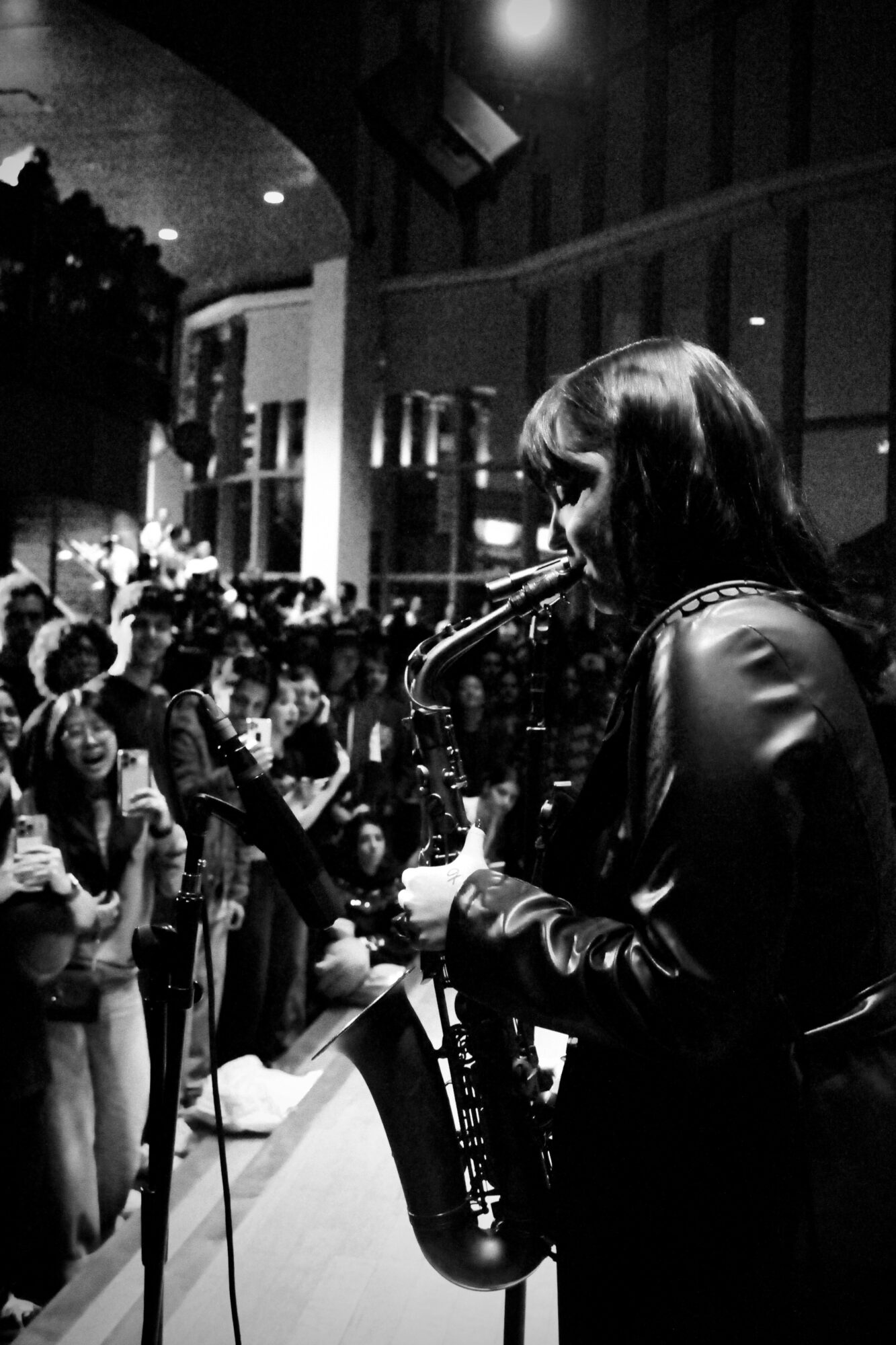 A woman playing a saxophone in a crowded indoor space with people watching.