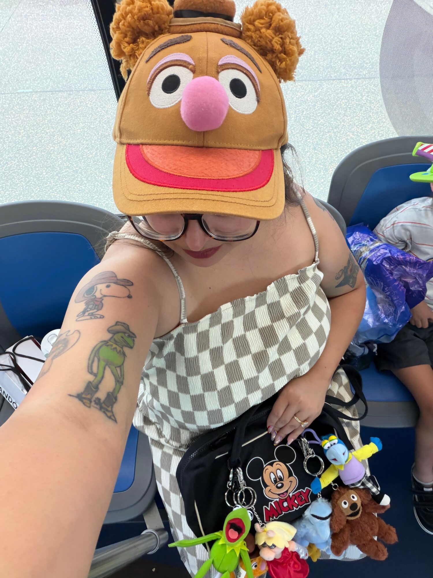 Person wearing a colorful animal hat with a pink nose, glasses, and a checkered top, sitting in a waiting area.