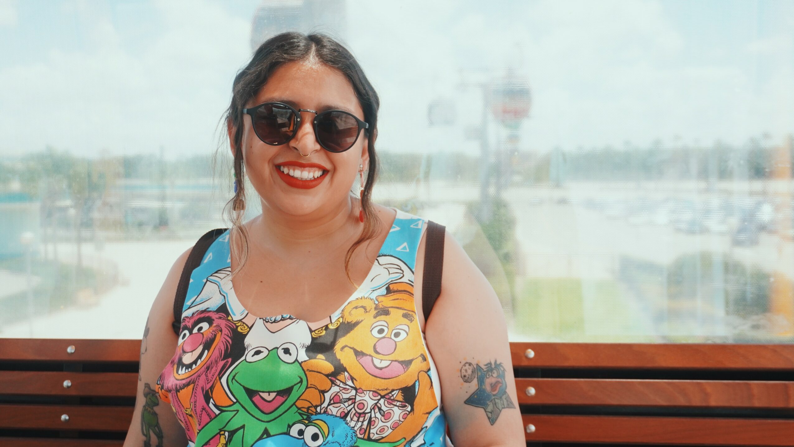 Smiling woman with sunglasses and colorful tank top sitting on a bench outdoors.
