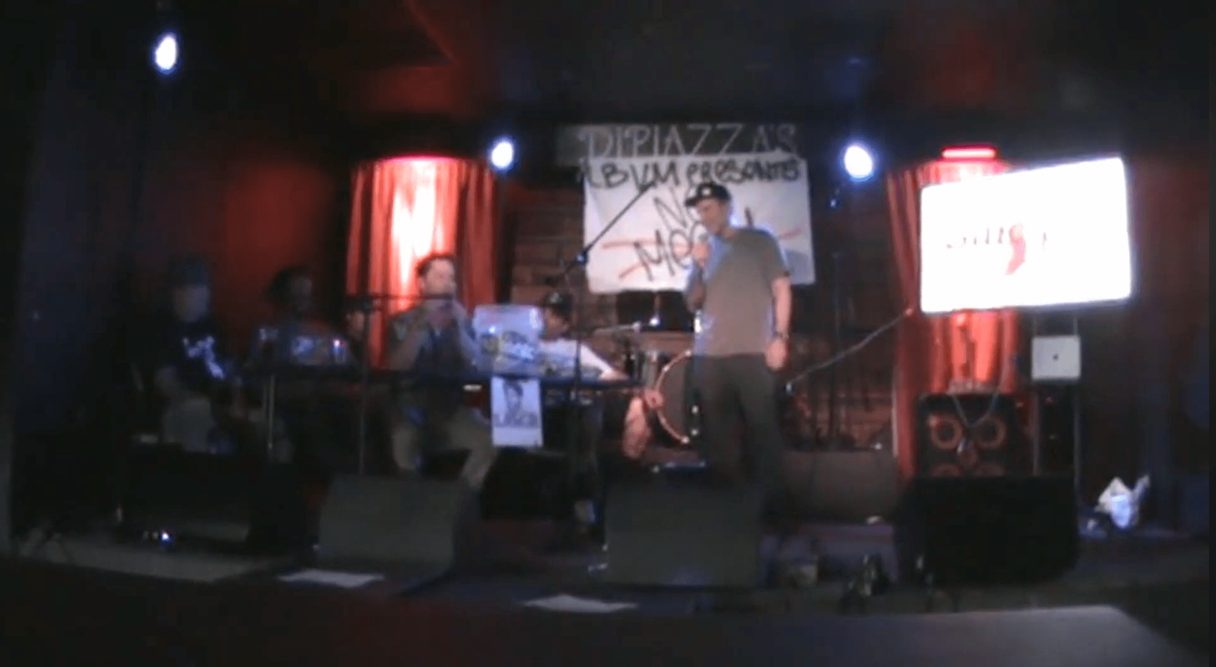 Band performing on stage with musicians and a singer, stage lights, and screens in the background.