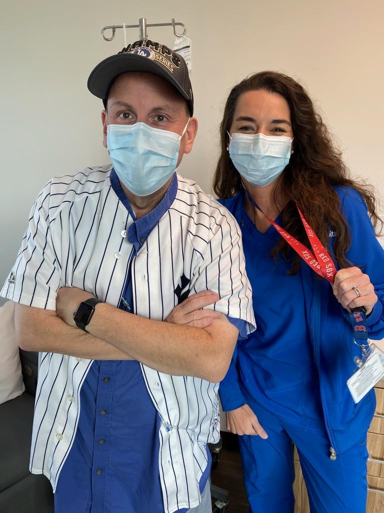 Two healthcare workers wearing masks, one in a striped uniform and the other in blue scrubs, standing indoors.
