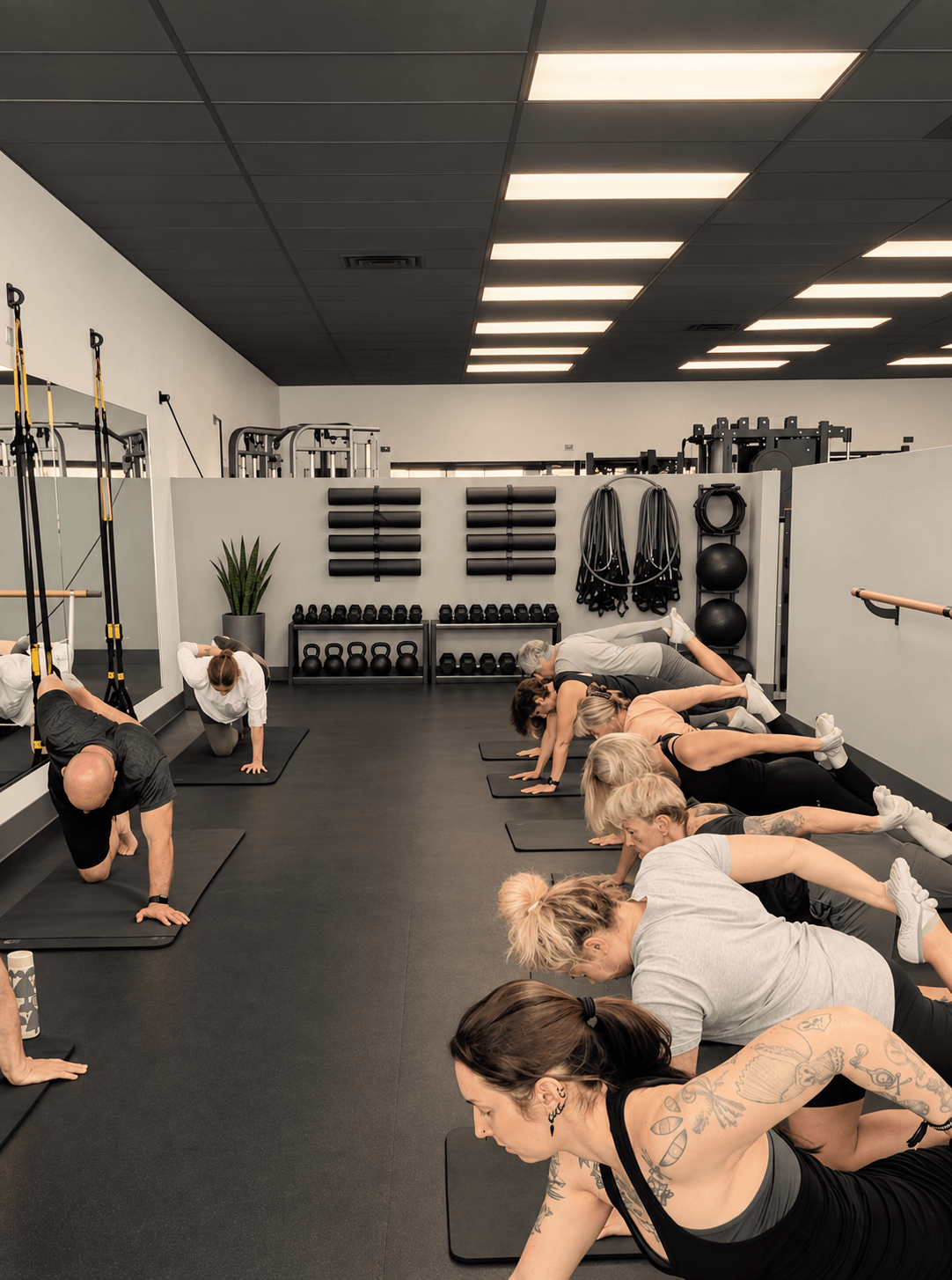 People doing yoga or stretching exercises on mats in a fitness studio with equipment on the wall.