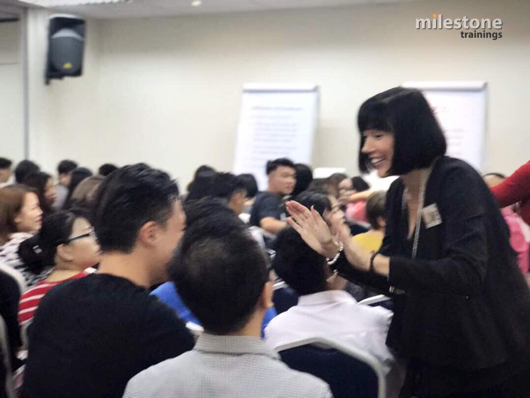 Woman smiling and clapping hands with a group of people in a conference room.