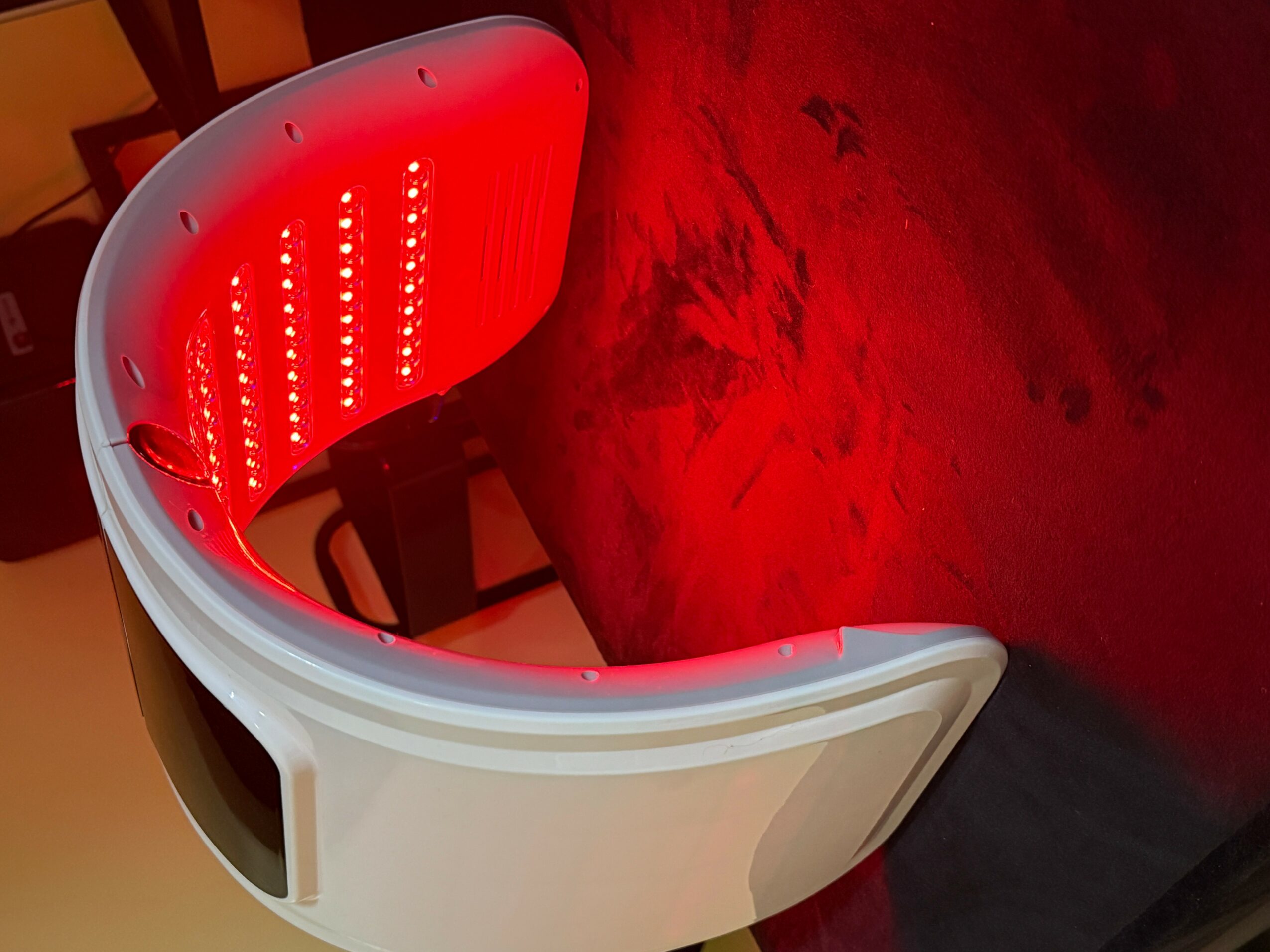 A white curved device with red LED lights on a dark surface, illuminated in a dimly lit environment.