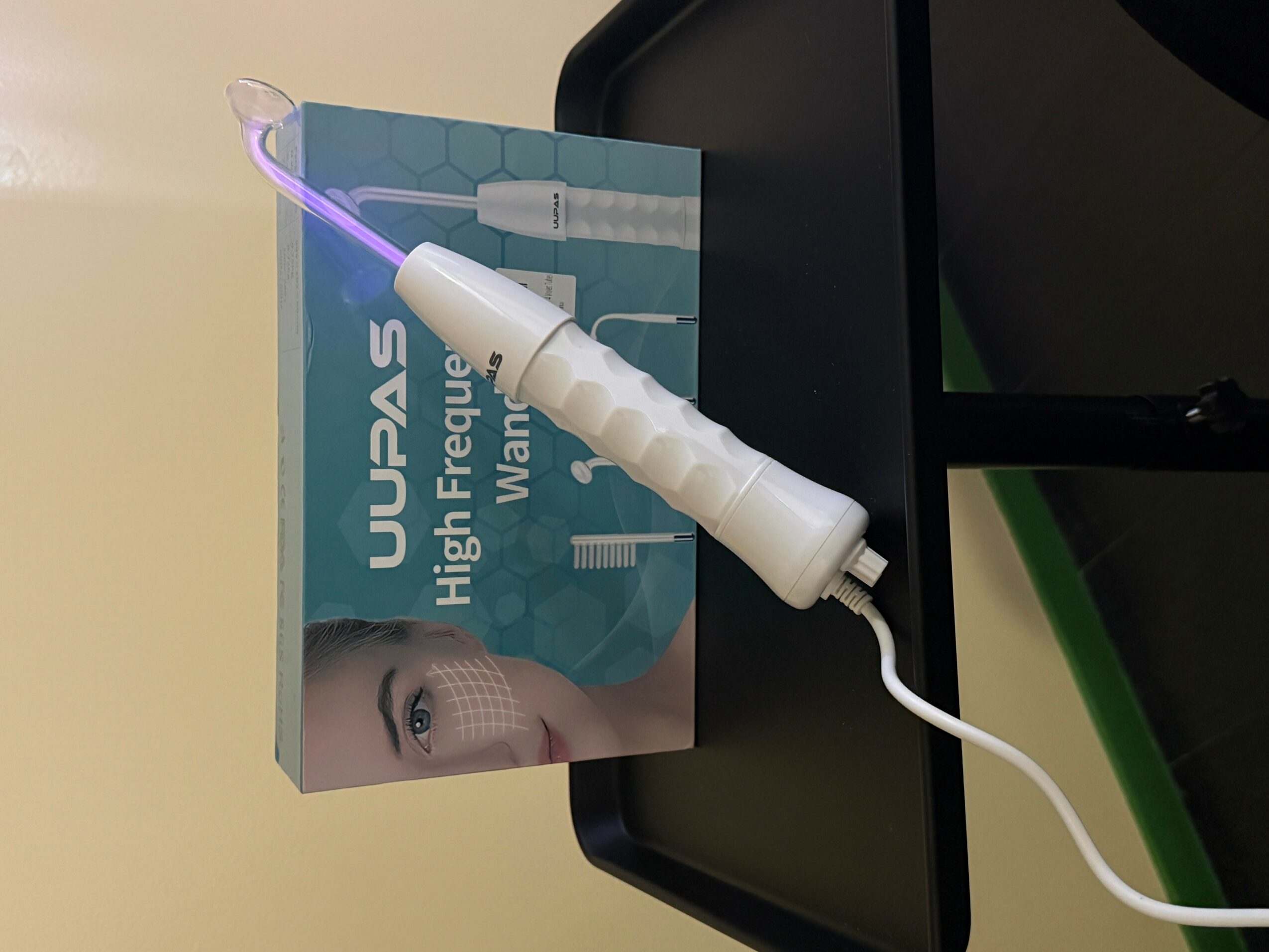 A white device with a purple light is connected to a box labeled 'UWAS High Frequency Wand' on a black surface.