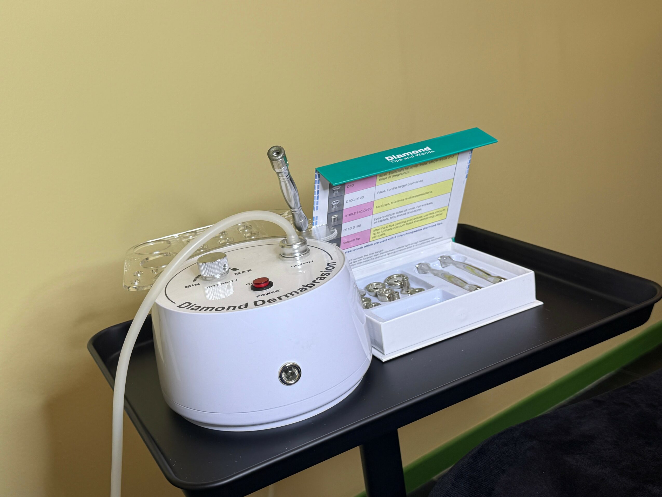 A dental curing light and a box of dental materials on a black tray, against a yellow wall.