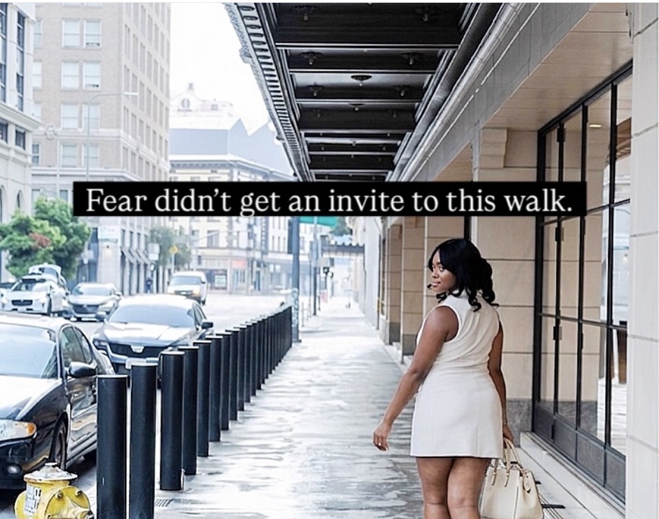 Woman in white dress walking on city sidewalk with buildings and cars, text overlay says 'Fear didn't get an invite to this walk.'