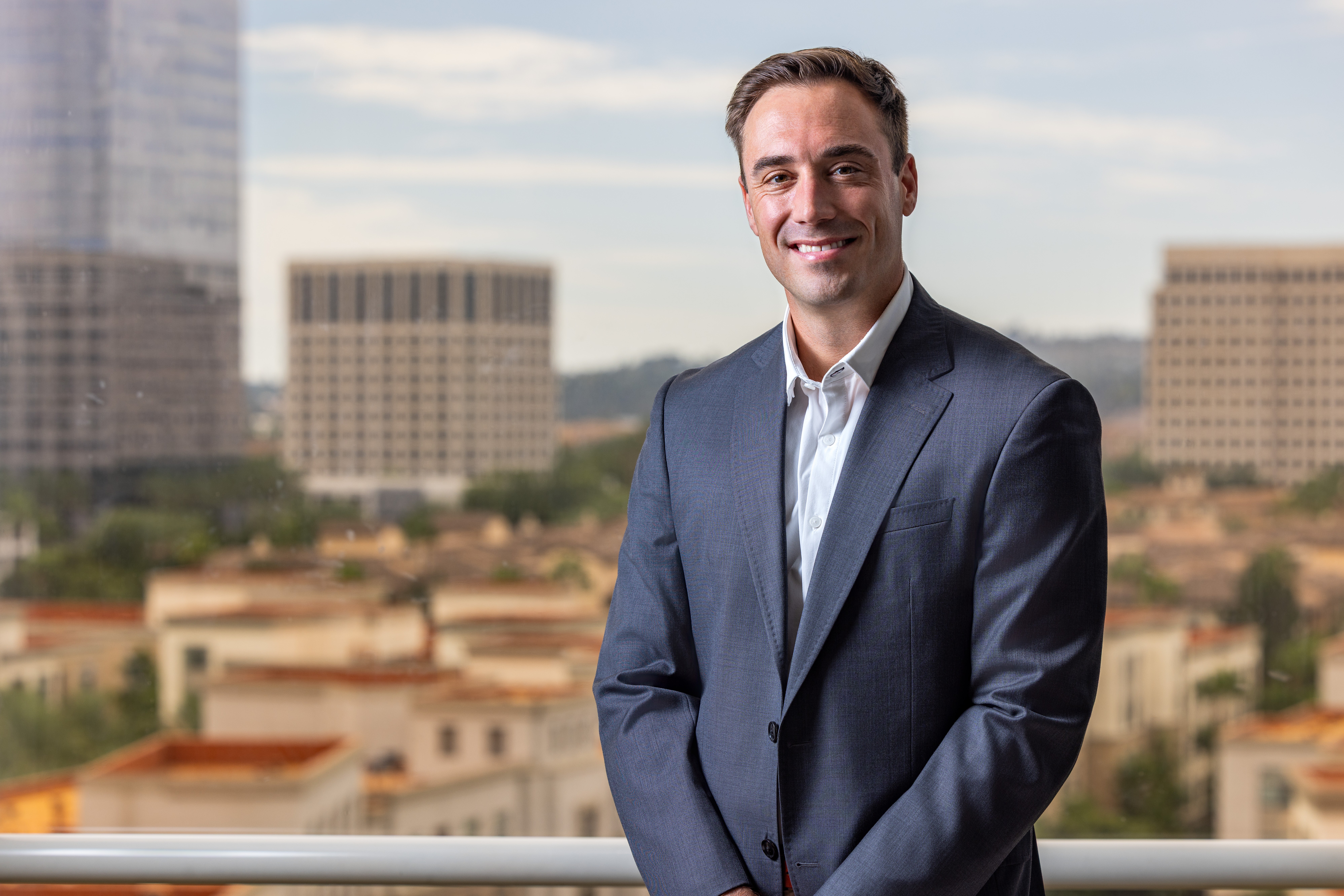 Man in a suit smiling outdoors with city buildings in background