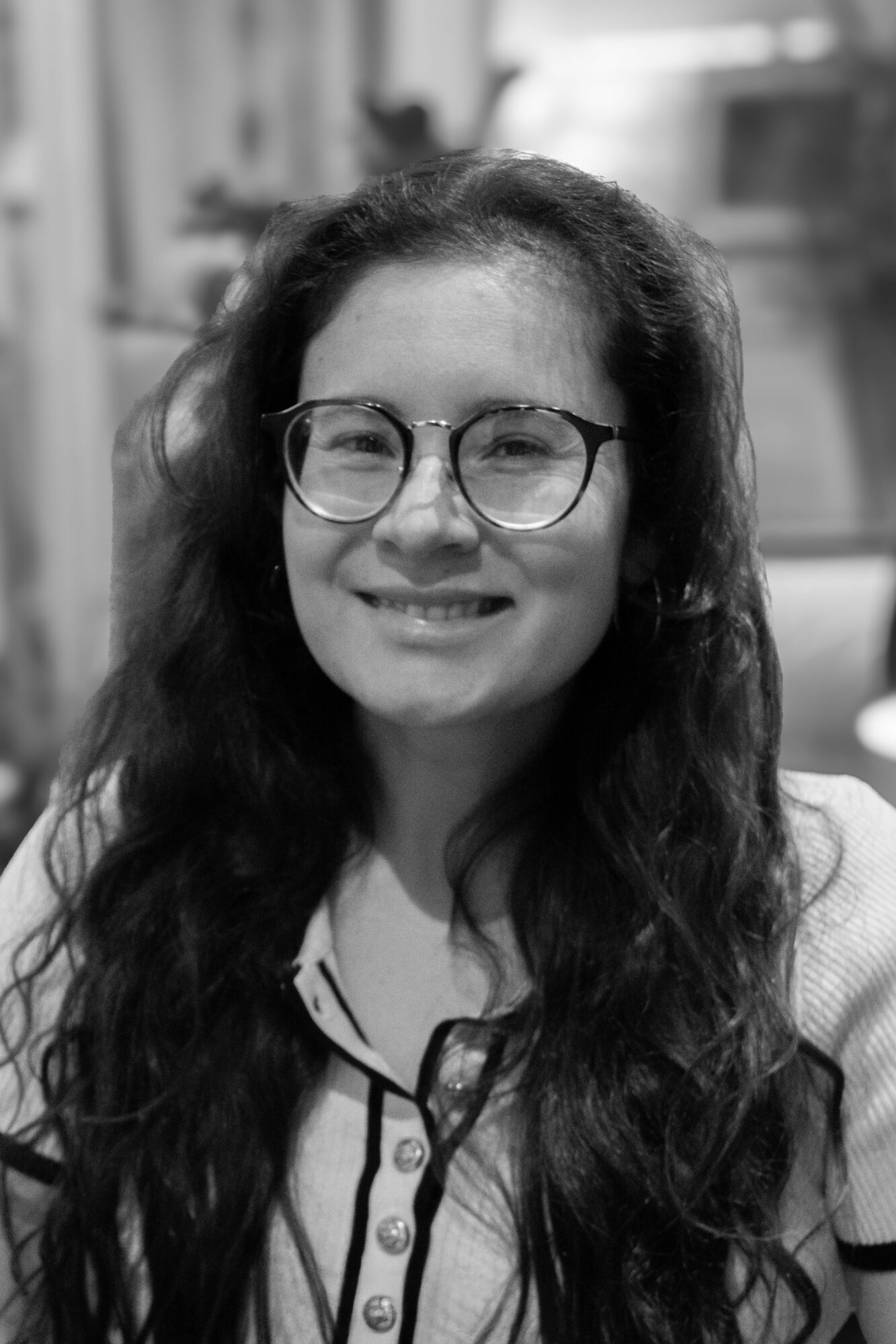 Young woman with glasses and long wavy hair smiling, wearing a striped shirt, in black and white.