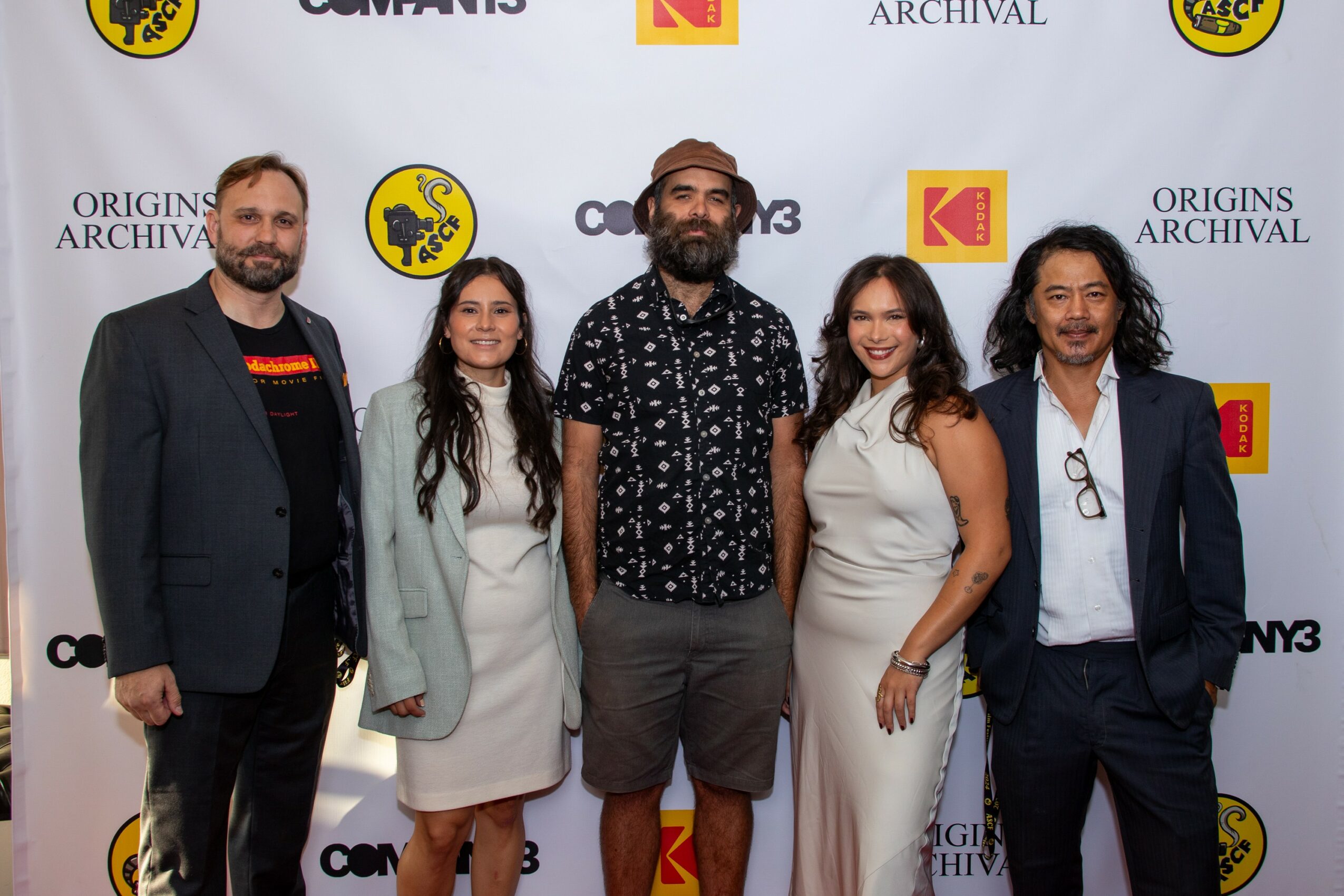 Group of five people standing in front of a backdrop with logos, smiling for the photo.