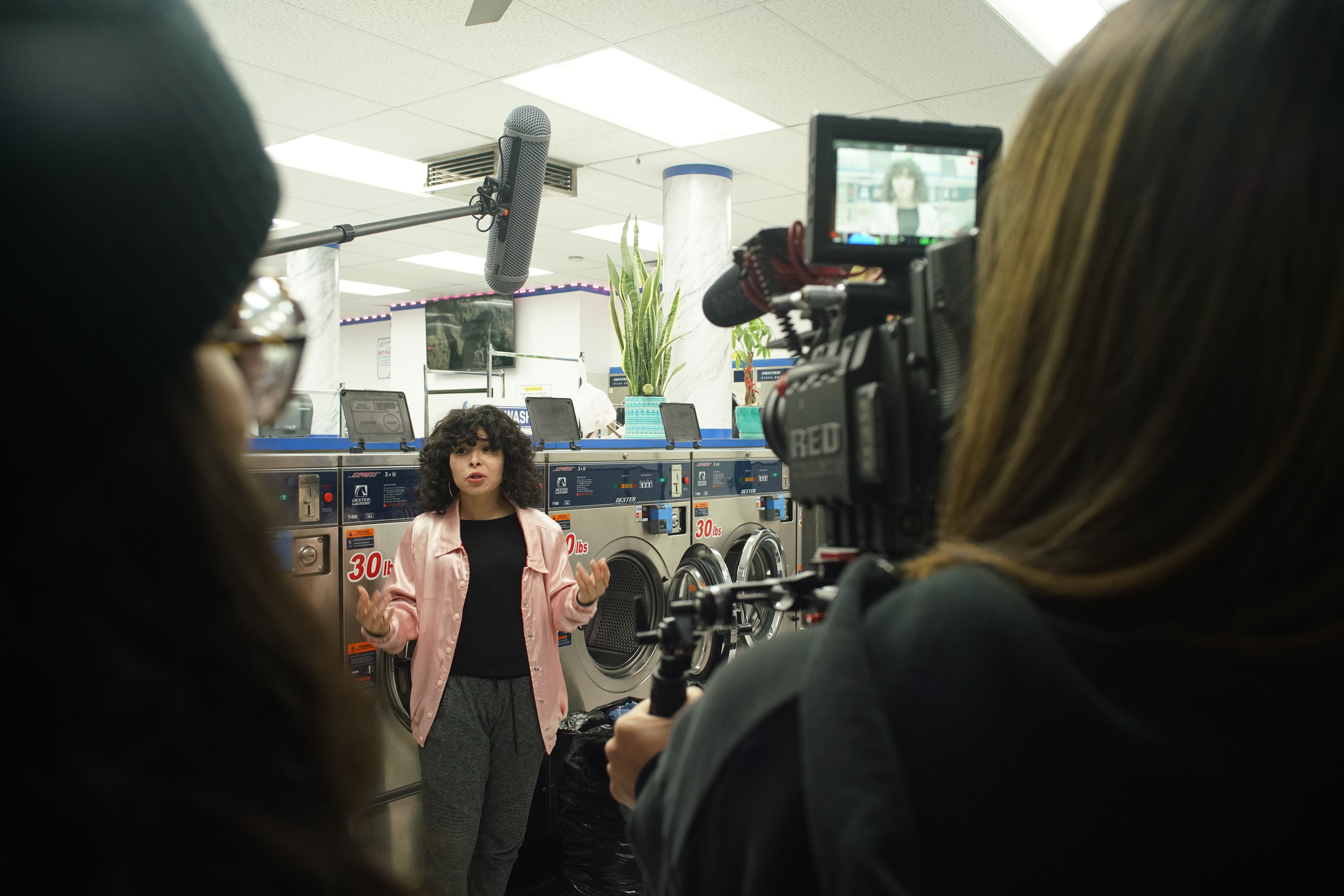 Woman being filmed in a store with washing machines, camera crew recording her, and other people nearby.